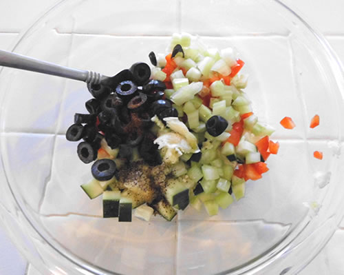 In a medium bowl, mix together the bell pepper, olives, celery, cucumber, garlic, chili powder, and pepper.