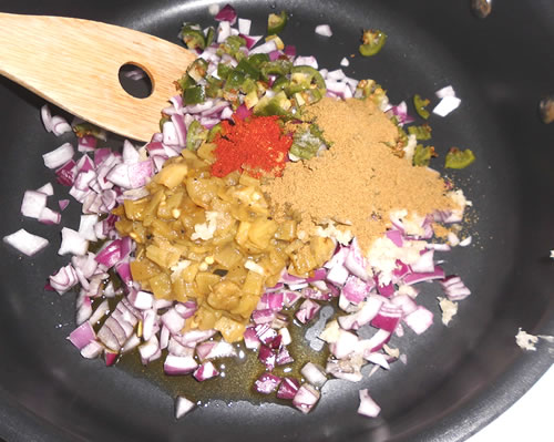 Heat the oil in a large pot; saute the onions, green chilies, garlic, jalapeno, cumin and chili powder for approximately 5 minutes or until the onion is tender.