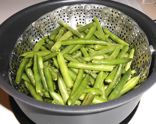 Steam the green beans for 10 to 15 minutes or until tender; remove and place into a large bowl.
