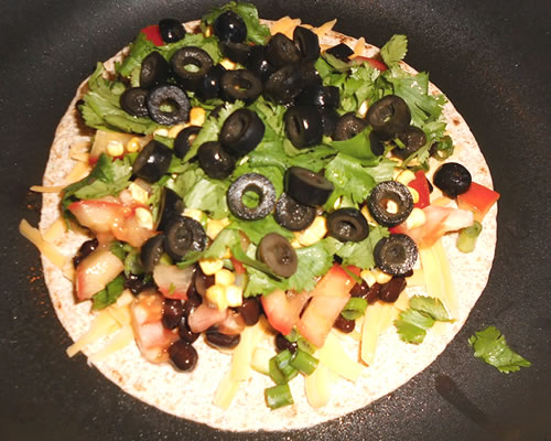 Lightly spray a large saute pan with cooking oil and heat over medium high; add one tortilla, the cheese, beans and the rest of the ingredients; top with the second tortilla.