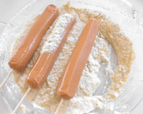 Insert a wooden skewer into the hot dog; roll the hot dog in the batter.