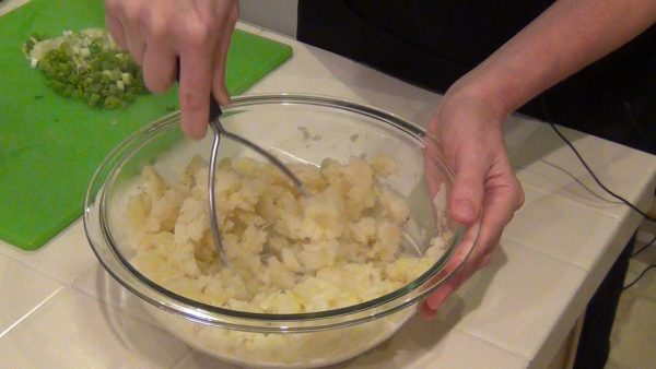 In a large bowl, partially mash the hot potatoes with a potato masher or a fork.