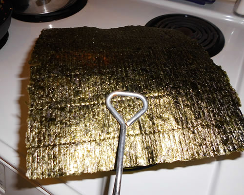Using tongs, hold the nori sheet over a burner and brown the sheet on both sides; crumble the sheet in a small bowl.