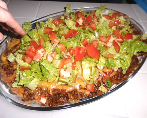 Add the shredded lettuce, tomatoes, green onions, and olives on top of the beans, crumble and cheese layer.