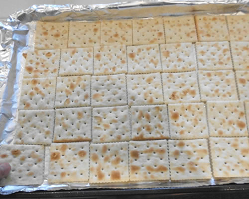 On a greased cookie sheet, place the saltine crackers in a single layer (approximately one package depending on the size of the cookie sheet).