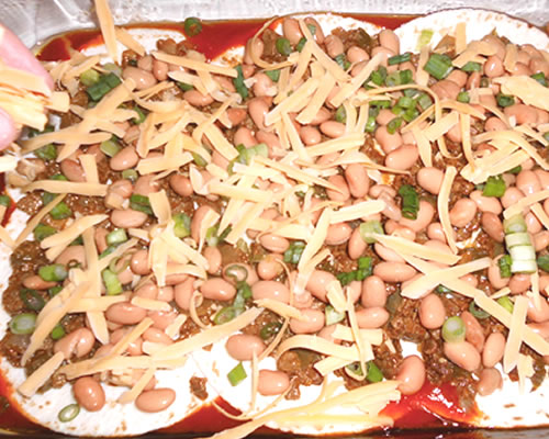 Coat the bottom of a 13 x 9-inch casserole dish (greased) with 1/3 of the enchilada sauce. Add 1/3 of the corn tortillas, 1/3 of the meatless crumble mixture, and 1/3 each of the beans, onion, cheese, and green chiles.